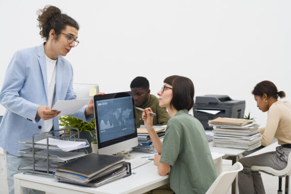 Team of diverse professionals collaborating in a modern office, analyzing data on a computer screen with documents and reports on the desk, CVAD training