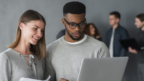 Two diverse professionals collaborating while viewing a laptop during a Citrix authorized training session, with blurred colleagues in the background in a modern office setting.