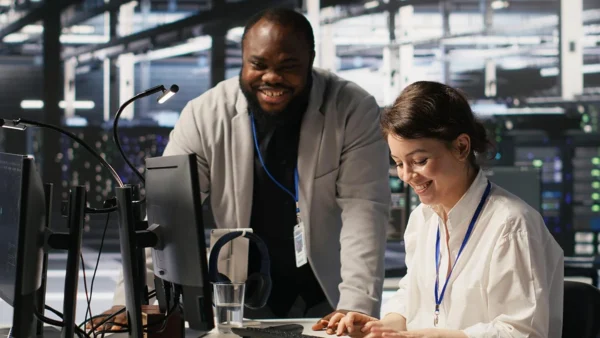 A network security instructor and trainee reviewing work at a computer in a server room Check Point Firewall.